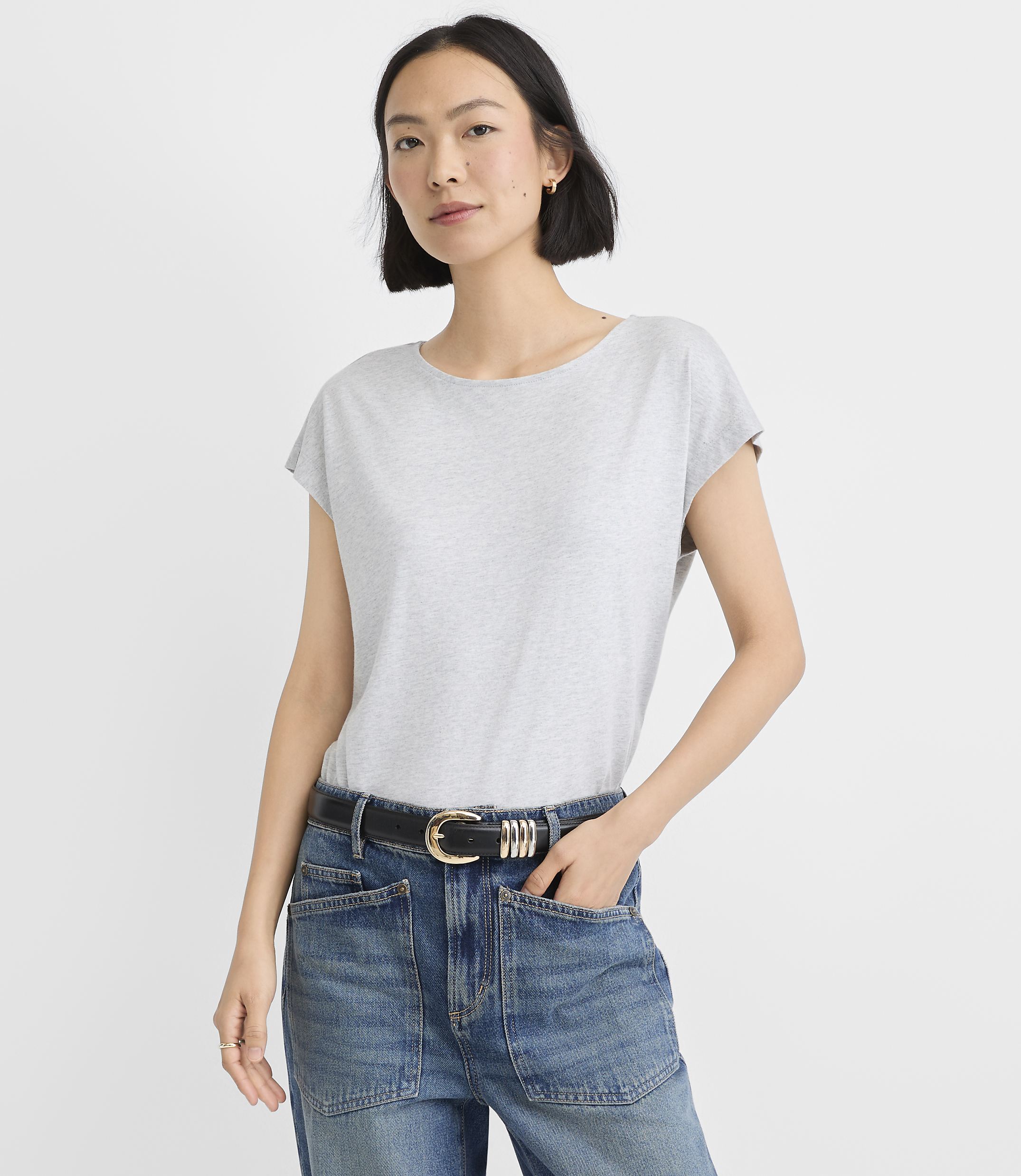 A woman in a grey t-shirt and a patterned denim skirt stands against a plain white background.