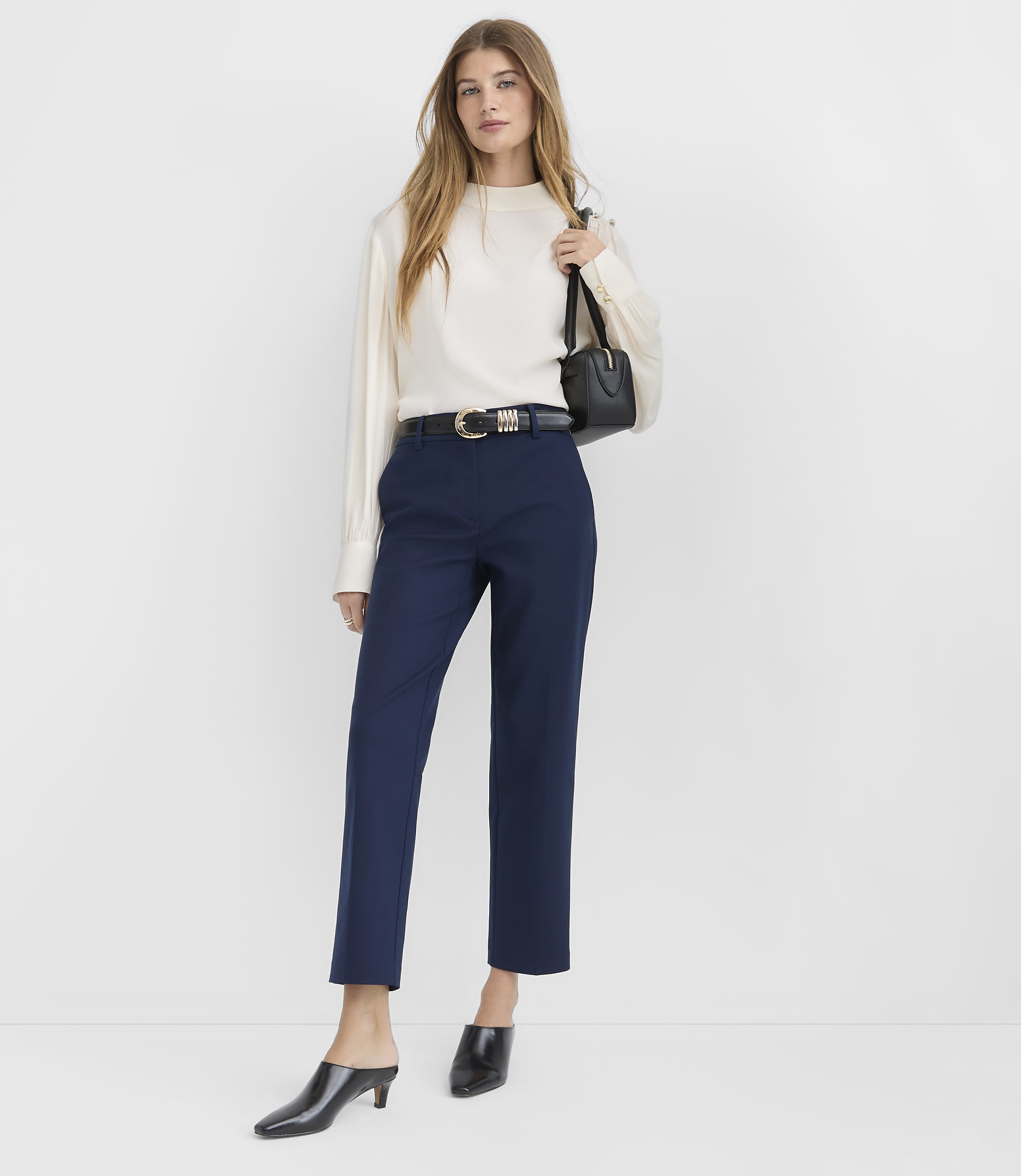 A woman in a denim jacket, patterned top, and navy pants stands against a plain white background.