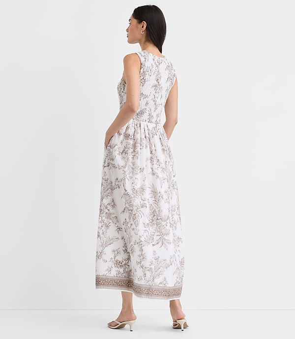 A woman wearing a white and gray floral print dress stands against a plain white background, her profile visible as she faces away from the camera.