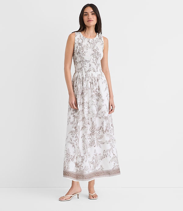 A young woman wearing a white and gray floral print dress stands against a plain white background, her expression serene and her posture relaxed.