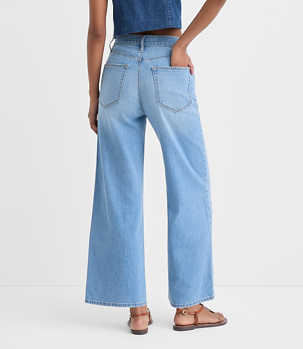 The image shows a person wearing light blue wide-leg denim jeans, standing against a plain white background.