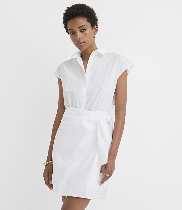A woman in a white shirt dress with a tie waist stands against a plain white background.