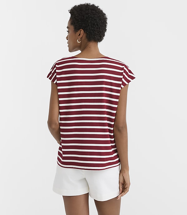 A woman in a striped shirt and white shorts stands against a plain white background.