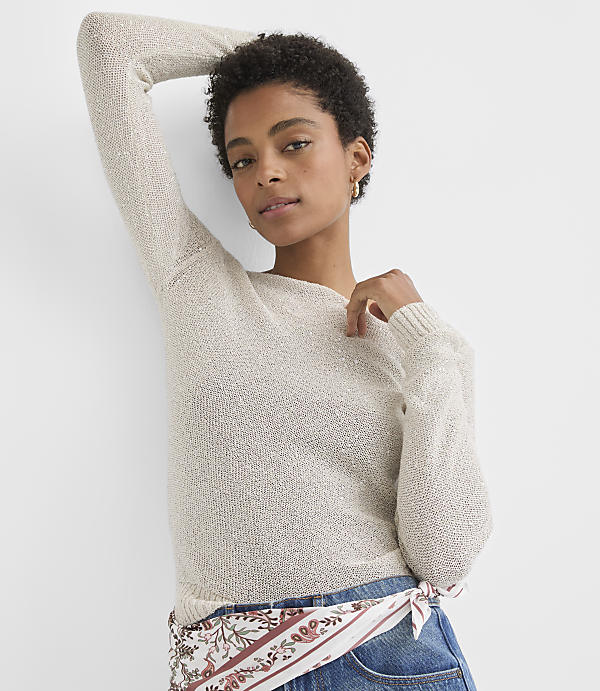 A woman in a light-colored sweater and jeans poses against a plain white background.