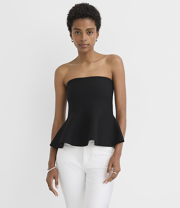 A woman in a black strapless peplum top and white pants stands against a plain white background.