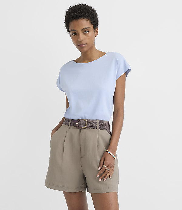 A woman in a light blue t-shirt and khaki shorts stands against a plain white background.