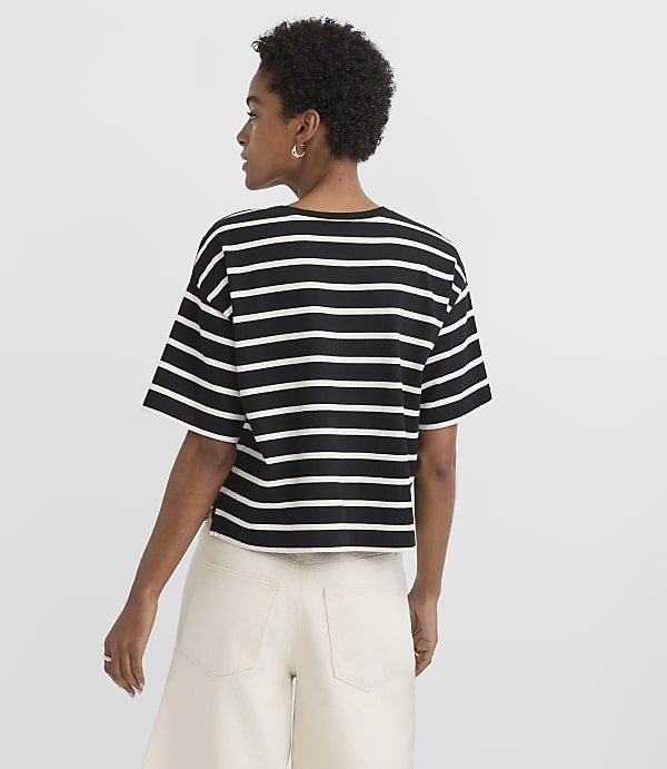 A woman in a striped t-shirt and light-colored pants stands against a plain white background.