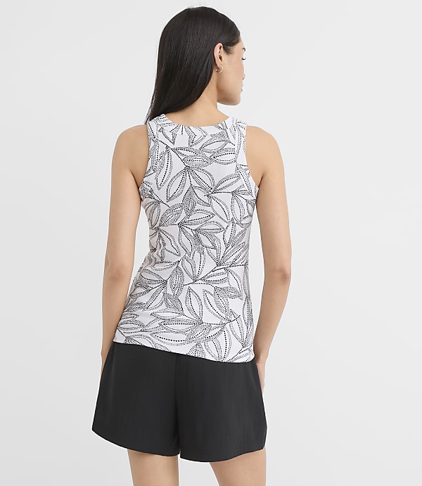 A woman in a leaf-patterned tank top and black shorts stands against a plain white background.