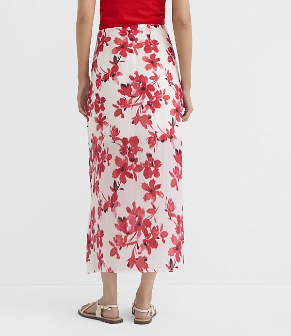 A person wearing a white skirt with red floral print stands on a plain white background.