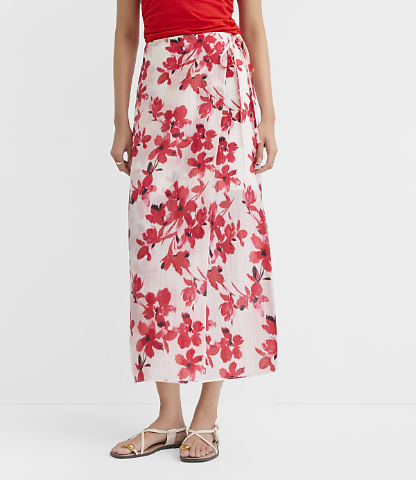 A woman in a red top and a white floral skirt with red flowers stands against a plain white background.