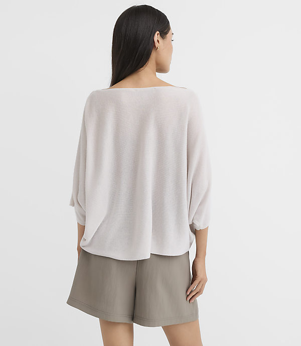 A woman in a light gray sweater and olive shorts stands against a plain white background.