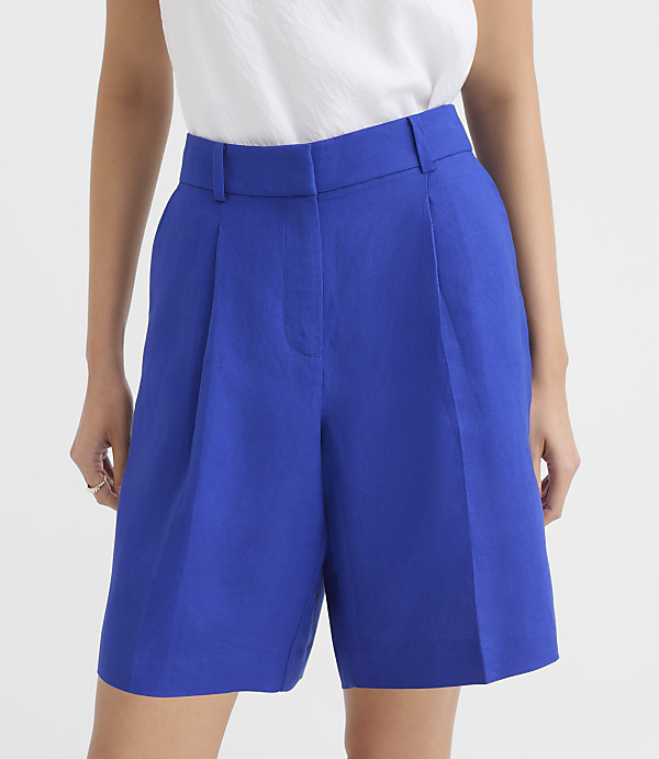 A person in the foreground wears bright blue pleated shorts and a white top, against a plain white background.