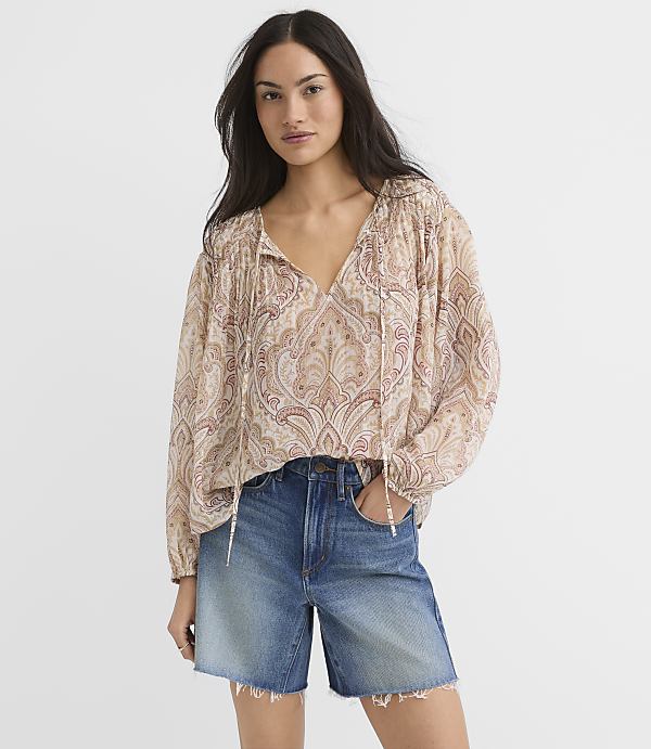 A woman in a patterned blouse and denim shorts stands against a plain white background.