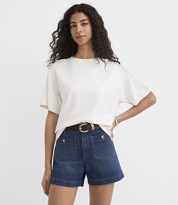 A woman in a white t-shirt and denim shorts stands against a plain white background.