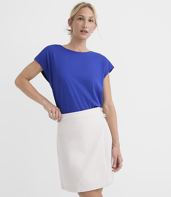 A woman in a blue t-shirt and white skirt stands against a plain white background.