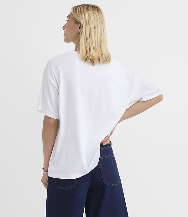 A woman in a white t-shirt and dark jeans stands against a plain white background.