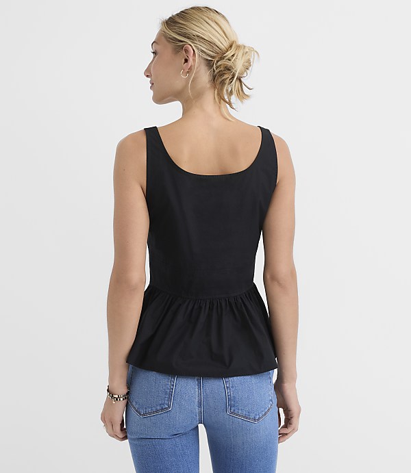 A woman in a black peplum top and blue jeans stands against a plain white background.