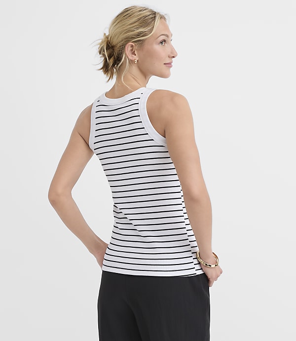 A woman in a striped tank top and black pants stands against a plain white background.