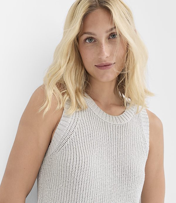 A blonde woman in a light gray knit top looks forward against a plain white background.