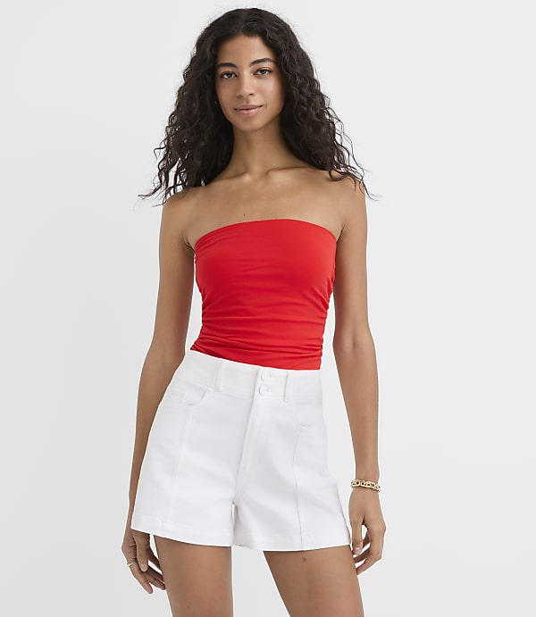 A woman in a red tube top and white shorts stands against a plain white background.