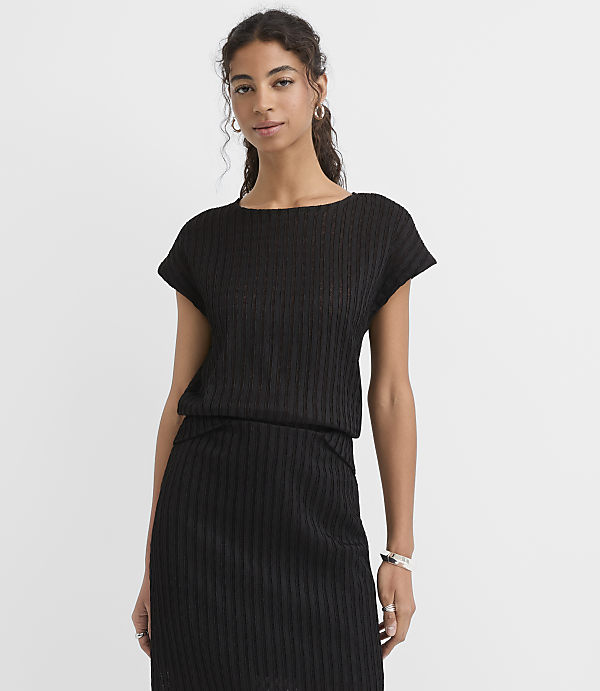 A woman in a black ribbed top and skirt stands against a plain white background.