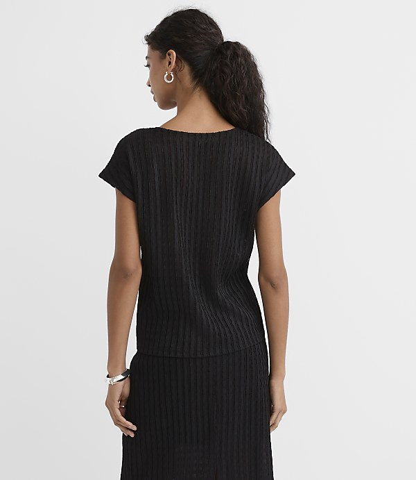 A woman in a black ribbed top and skirt stands against a plain white background.