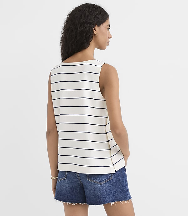 A woman in a striped tank top and denim shorts stands against a plain white background.
