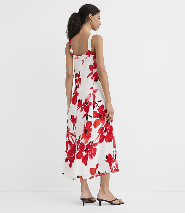 A woman in a white floral dress stands against a plain white background.
