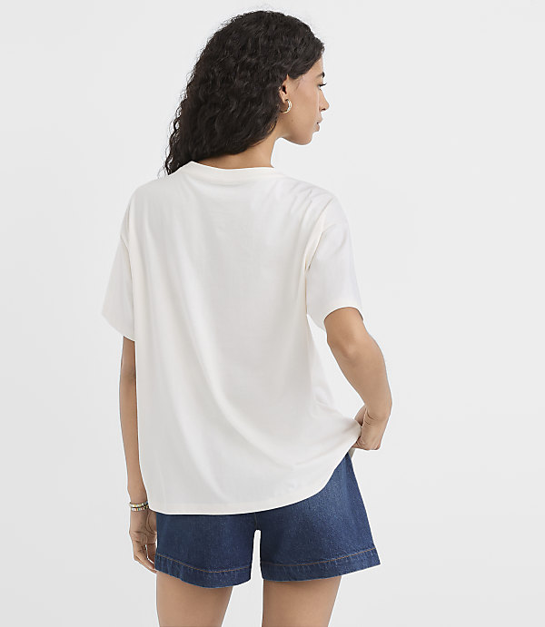 A woman in a white t-shirt and denim shorts stands against a plain white background.