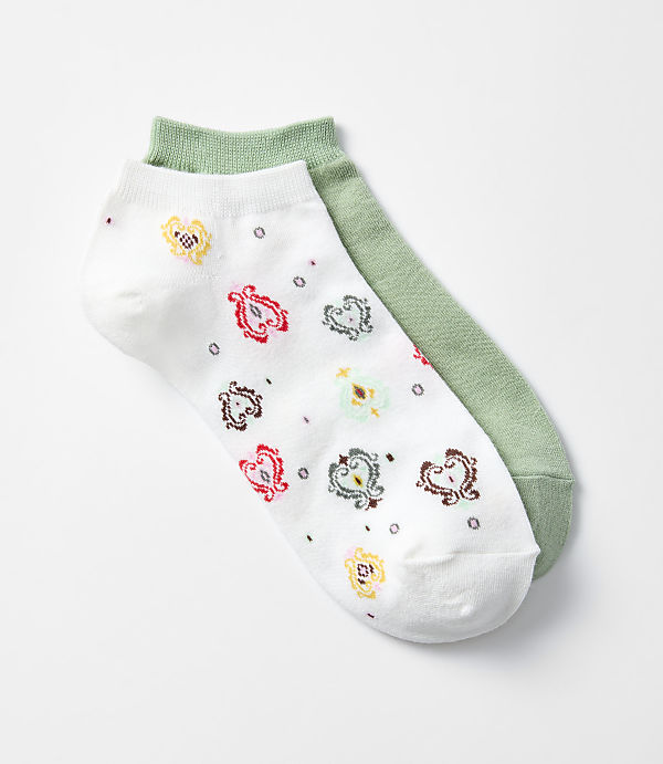 A pair of ankle socks, one white with a colorful paisley pattern and the other solid green, lie on a plain white background.