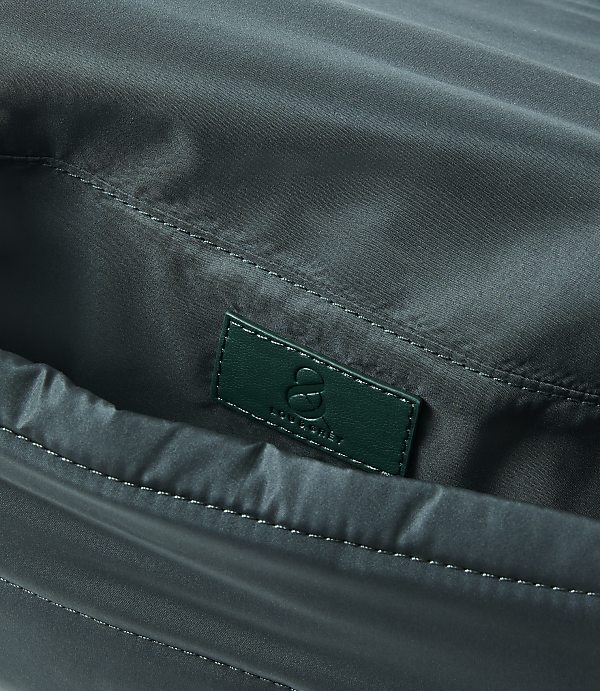 A close-up of a dark green fabric bag's interior reveals a small, embossed green leather tag with a logo in the foreground, against the softly creased, shiny fabric of the bag's lining in the background.