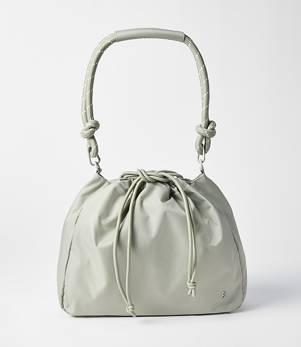 A light gray drawstring bag with a curved handle rests on a plain white background.