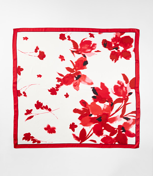 A white silk scarf with a vibrant red floral watercolor print and a red satin border is displayed against a plain white background.