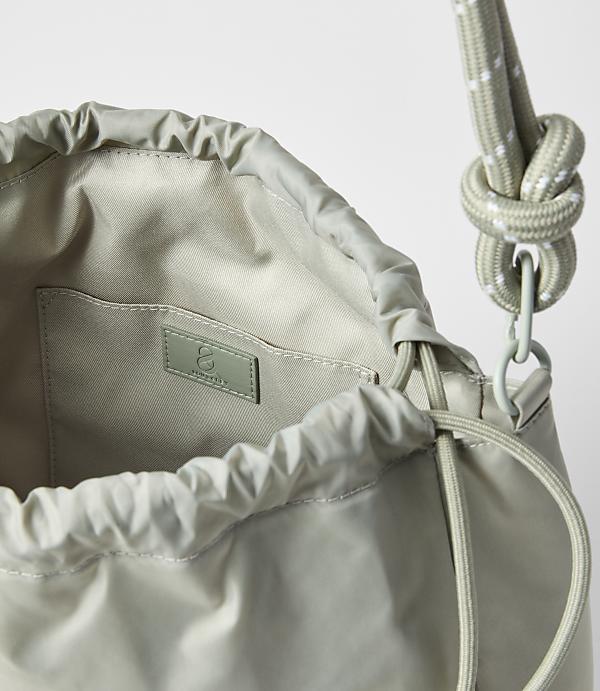 A light green drawstring bag with a white-speckled rope strap is shown against a plain white background.