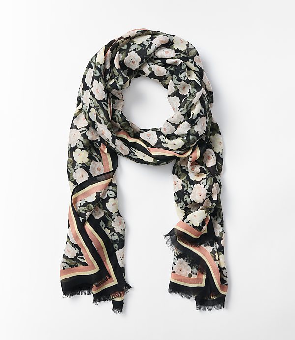 A floral scarf with a black background and pink roses is laid out on a white surface.