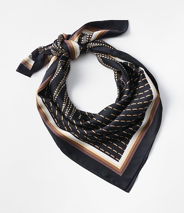 A black silk scarf with a geometric pattern of dots and lines in brown, beige, and white is tied in a knot against a plain white background.