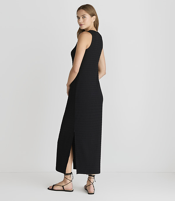 A woman in a black maxi dress with a slit stands against a plain white background.
