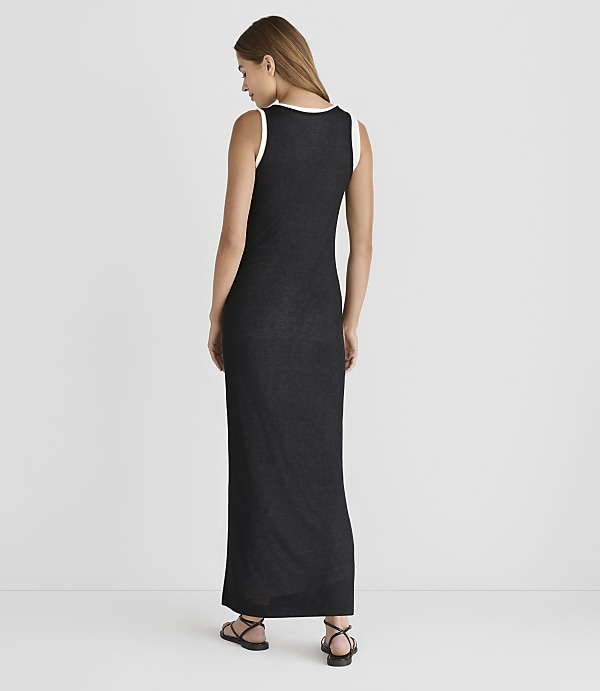 A woman in a black maxi dress with a white trim stands against a plain gray background.