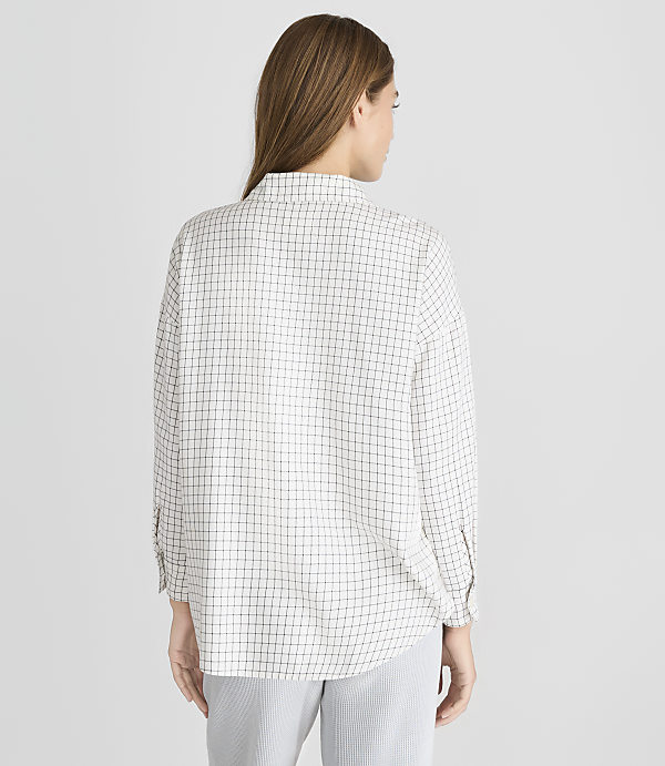A woman wearing a checkered shirt and striped pants stands against a plain gray background.