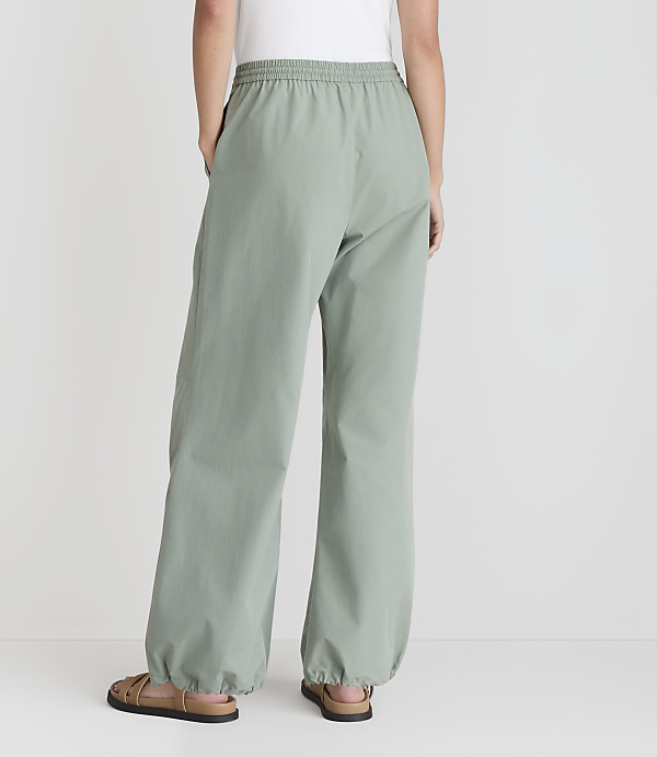 A person wearing loose-fitting, light green pants with elastic cuffs stands with their back to the camera against a plain white background.