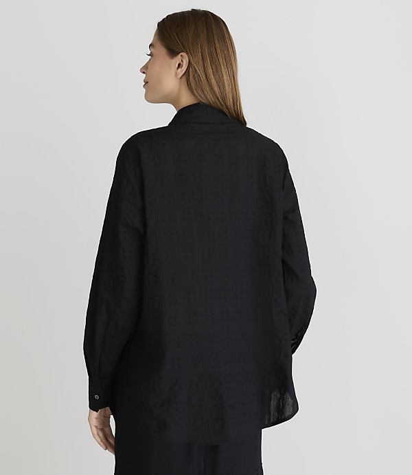 A woman in a black textured shirt stands against a plain gray background.