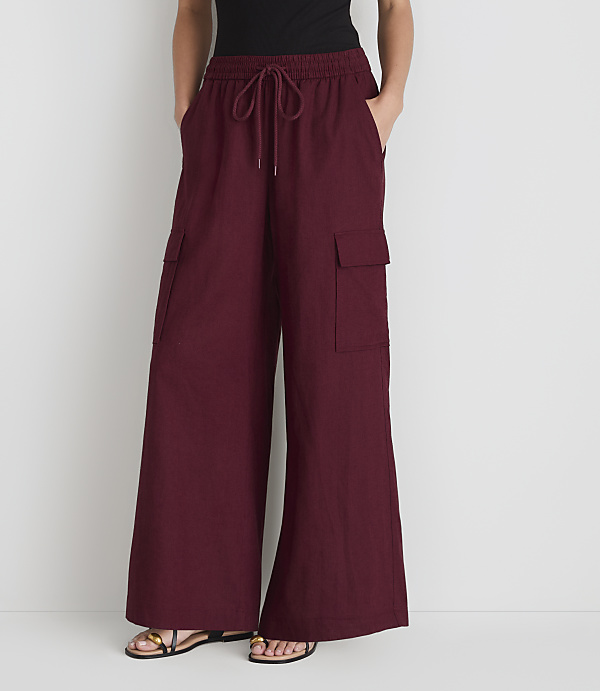 A person stands in front of a plain white background, wearing loose-fitting maroon cargo pants with their hands in their pockets.