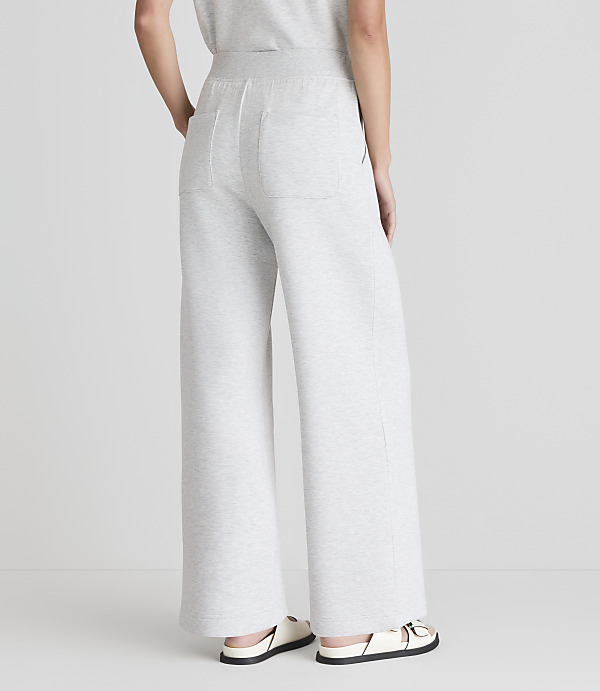 A person wearing light gray wide-leg sweatpants and white sandals stands against a plain white background.