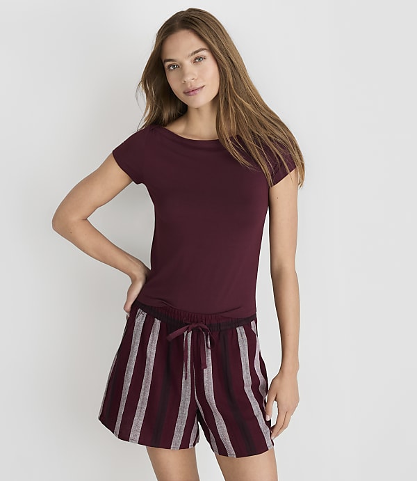 A woman in a maroon t-shirt and striped shorts stands against a plain white background.