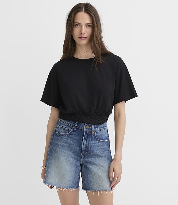A woman in a black t-shirt and denim shorts stands against a plain white background.