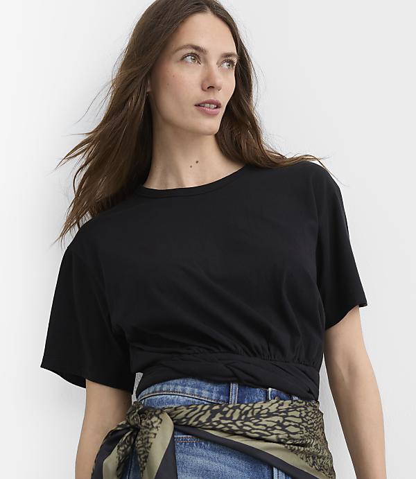 A woman in a black t-shirt and jeans is shown against a plain white background.