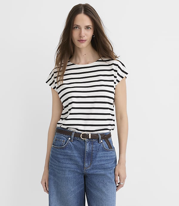 A woman in a striped shirt and jeans stands against a plain white background.