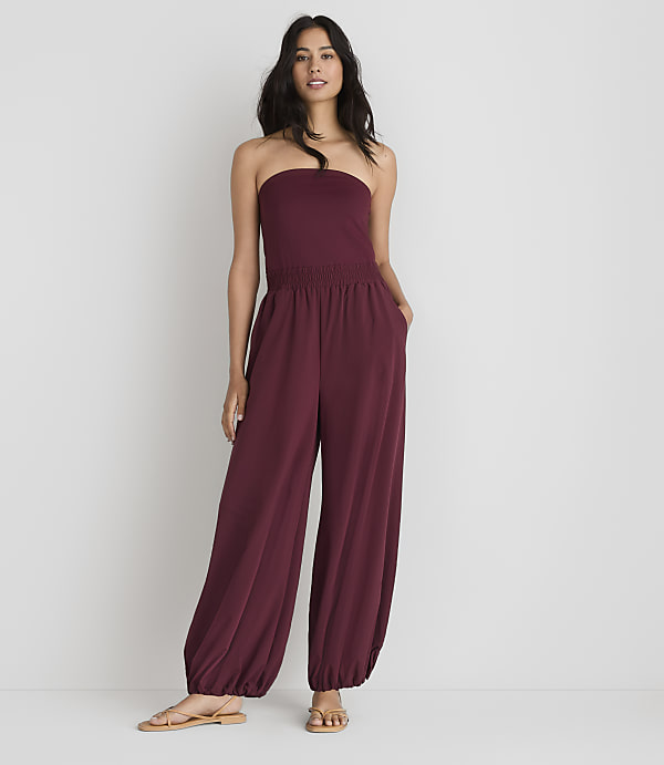 A woman in a maroon strapless jumpsuit stands against a plain white background.