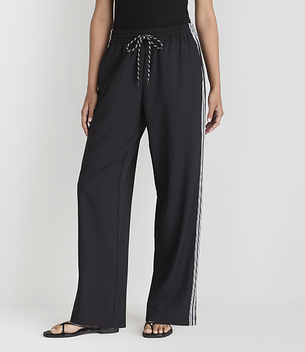 A person stands in black wide-leg pants with white stripes down the sides, against a plain white background.