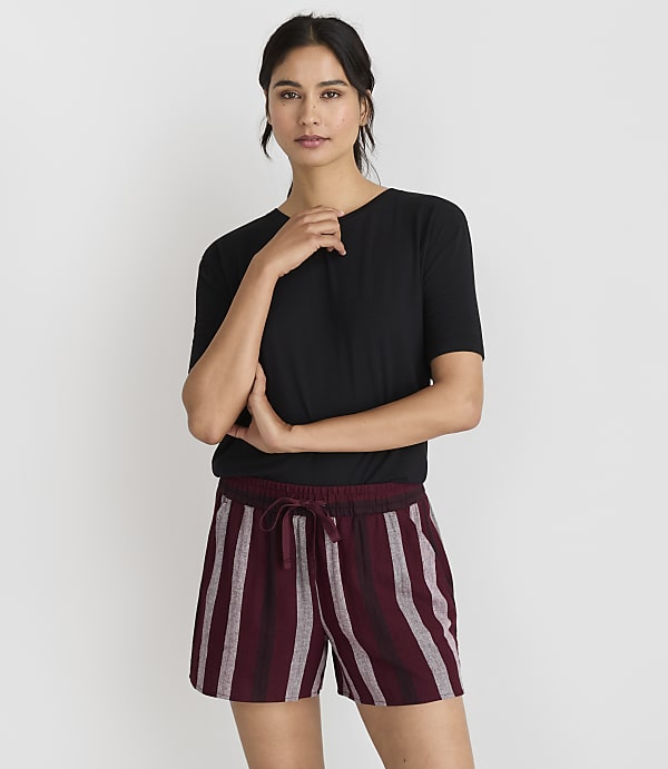 A woman in a black t-shirt and striped shorts stands against a plain white background.